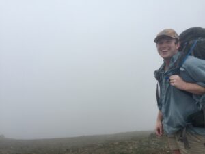 A hiker smiles before a bank of fog in the Chugach Range, Alaska