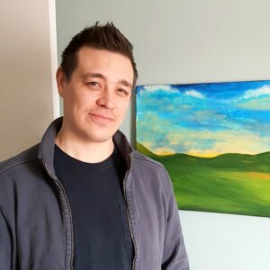 Ryder is standing next to a landscape painting.