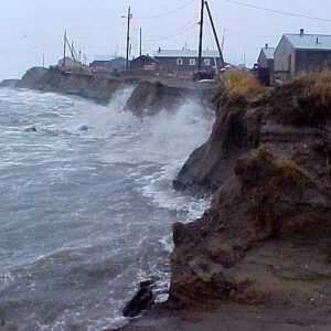 Photos of waves watching against an eroding wall of dirt with house precariously close to the edge. Climate change harms Alaska's coastal communities.