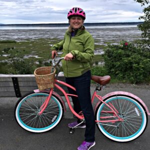 Tracy posing with her bike with the mud flats of Cook Inlet behind her.