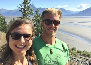 Kat and Dave take a photo with the Turnagain Arm mudflats and blue skies behind them.